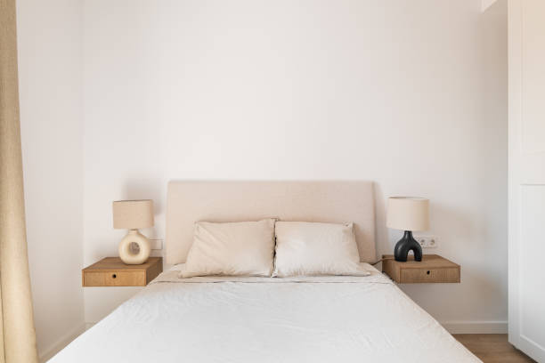 istock Horizontal shot of a double bed with white pillows and bedspread bedside tables sconces on a background of white wallpaper and a closet. Concept of a new apartment for a young family 1871081664