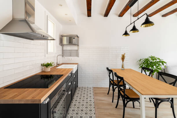 istock Long dining table with four chairs next to a kitchen island with a build in stove and extractor hood with white walls and renovation beams in a newly built house. Copyspace 1871081673