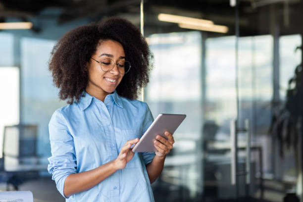 Young beautiful successful woman at workplace inside office with tablet computer in hands, female programmer testing new app, happy smiling