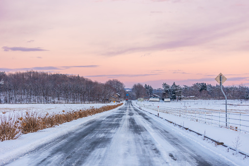 A rural countryside road covered with ice and snow in North Japan at sunset.