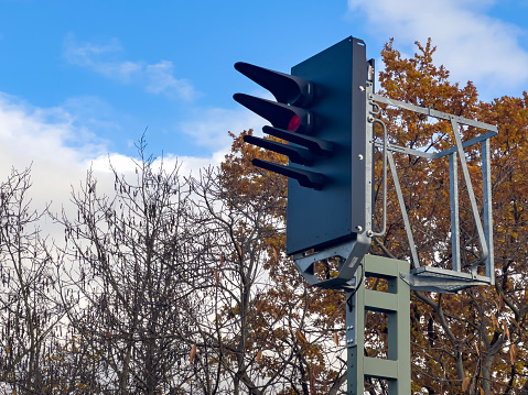 Outdoor subway station signs and light tower in nature with colourful autumn trees. Traffic light at level crossing. German road signs.