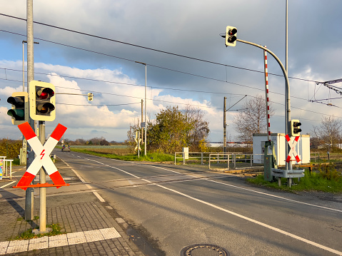 Outside the tube station, train barrier warning symbol: German road signs with traffic lights at level crossing and open gates. Multiple red and white railway icon with junction against a green landscape and cloudy sky.