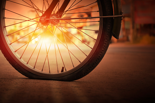 An old bike that has back flat tire parked by the urban road in the evening of the day and waited to fix later. Colour and lens flare edited. Soft focus