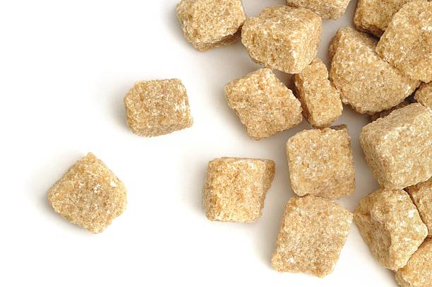 A close up shot of unrefined demerra sugar lumps scattered across a white background.