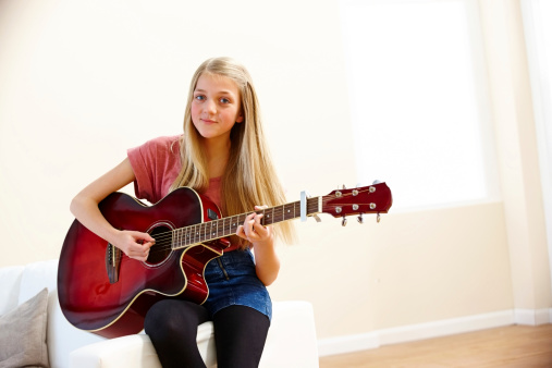 Image of pretty young girl sitting on sofa playing guitar - Indoors