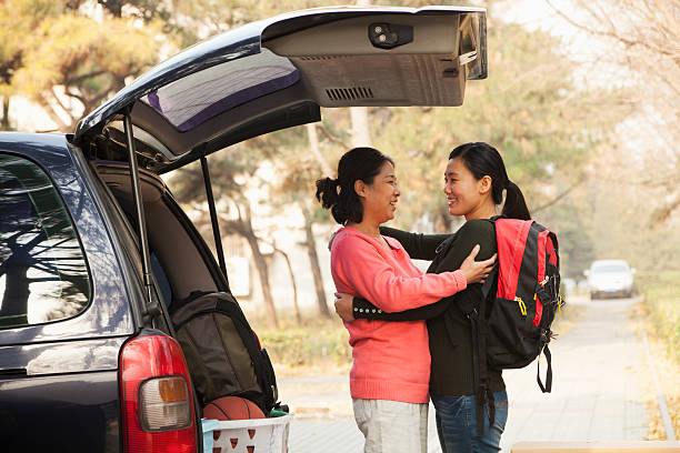 Mother and daughter embracing behind car on college campus Mother and daughter embracing behind car on college campus college student and parent stock pictures, royalty-free photos & images