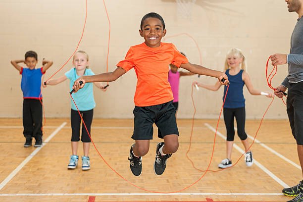 Diverse group of elementary children jumping rope Smiling boy is skipping rope.  The boy in the foreground is shown while jumping in the air, and there are three other children with ropes in the background.  There is an adult on the right side of the photo. skipping stock pictures, royalty-free photos & images