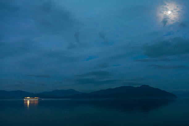 Cruise ship approaches Glacier National Park under full moon.