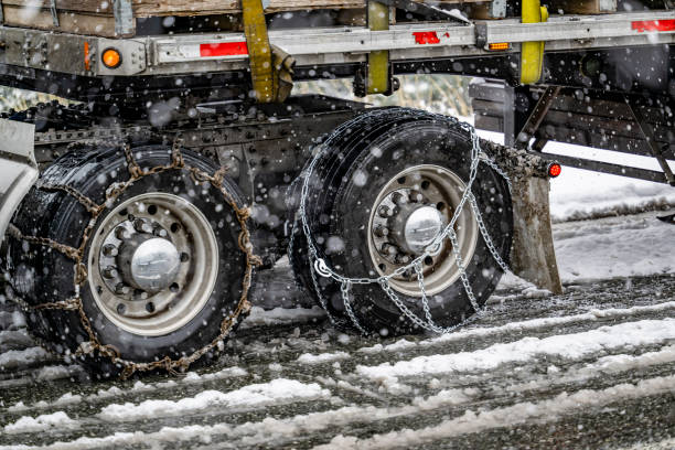 istock Properly and poorly secured chains for better grip on slippery road surfaces on wheels of the drive axles of semi truck carrying cargo on flat bed semi trailer in winter weather during snow storm 1871278290