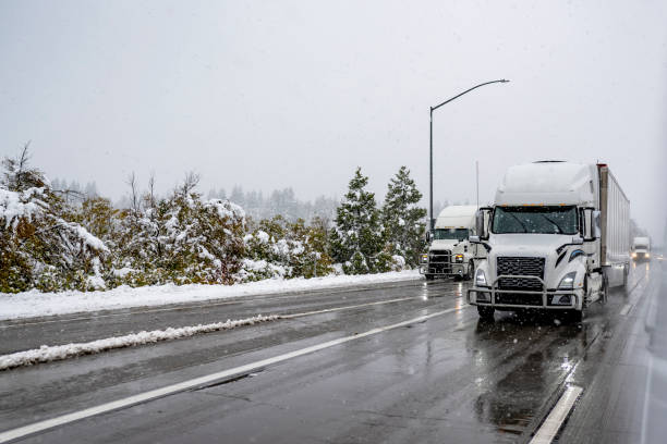 istock White big rig semi trucks with turned on headlight transporting cargo in semi trailer running on the winter highway road with wet slippery surface at snow storm time 1871280919