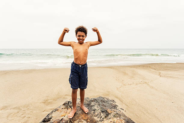 young boy flexionar los músculos en la playa - macho little boys flexing muscles human muscle fotografías e imágenes de stock