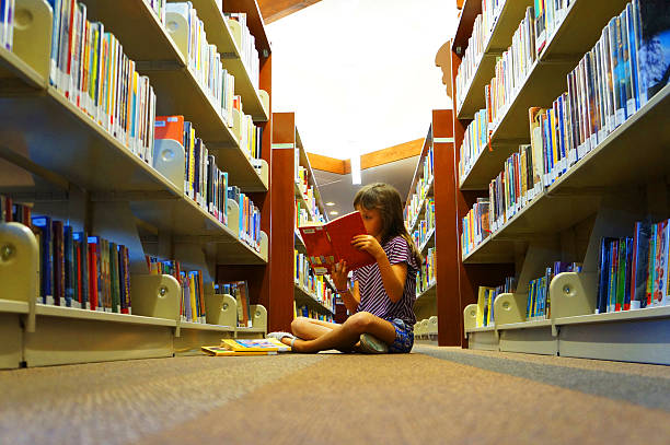 Little girl reading a book in school library