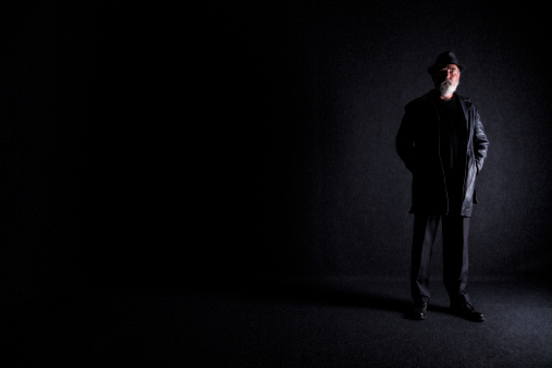 Studio shot of an older man, dressed in dark clothing, standing in a dark room - with plenty of copy space.