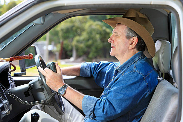 Worried farmer in vehicle listening to message A worried, mature stockman with bush hat listens to a radio message inside his work vehicle. He has his radio handset in his hand and a stock whip is visible on the dashboard. Strong light coming through windscreen onto his face. Can be flipped horizontally for use in Europe and North America. No logos, labels visible. old person listening to radio stock pictures, royalty-free photos & images