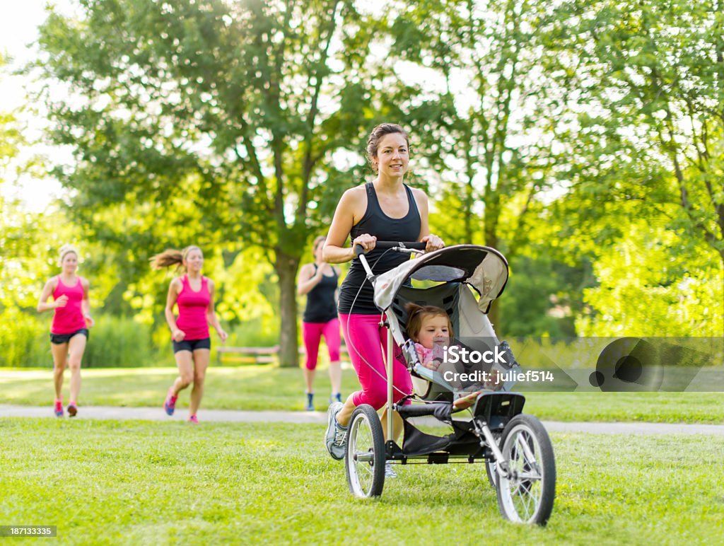 Mother running in the park Woman pushing her little girl in a toddler while running in nature with friends Marathon Stock Photo