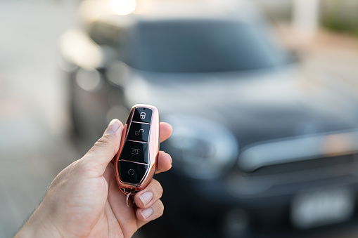 The driver hand is holding a keyless key to unlocking the car, photo with  luxury car as blurred background. Ready for driving concept scene.