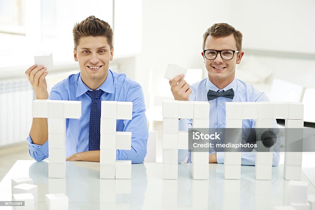 Successful team building Two handsome businessmen sitting behind the word "TEAM" made of white toy blocks 20-29 Years Stock Photo