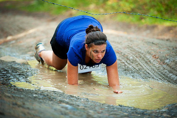 A woman in an obstacle race crawling through mud and barb wire