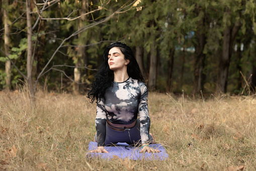 A woman practices yoga alone in the forest.