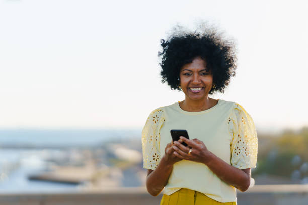 istock African woman smiling using phone outdoors during sunset 1871463502
