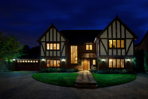 an evening view of a luxury mock-Tudor home taken a little while after sunset in order to expose the deep blue sky. All of the light of the house have been turned on. Bright white external lights at the front of the house and pillar lights (out of view) around the driveway have also lit up the lawn. This is NOT an HDR image. 