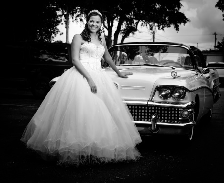 quinceanera wearing a traditional dress posing in front of an american car from the 50s