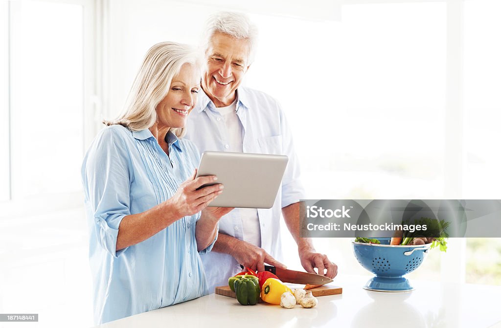Couple Using Tablet Computer In Kitchen Happy senior couple checking out recipe from tablet computer while cooking in kitchen. Horizontal shot. 60-69 Years Stock Photo