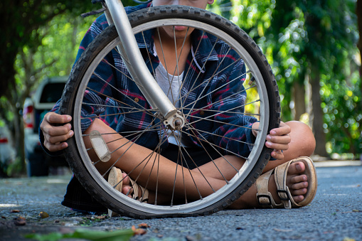 Closeup front wheel of bicycle which is flat and broken of asian boy behind, soft and selective focusใ