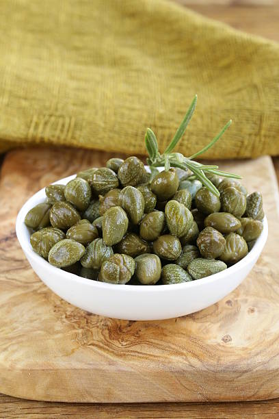 istock Pickled capers in white bowl on wooden table 187150647