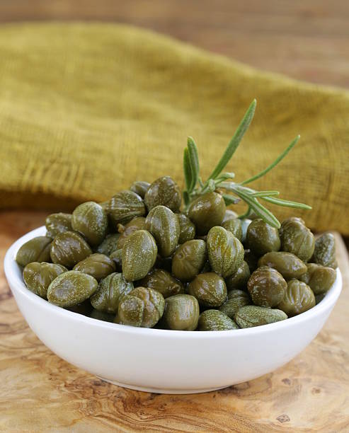 istock Pickled capers in white bowl on wooden table 187151456