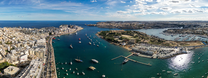 Discover Sliema and Valletta in Malta overlooking the Mediterranean Sea with boats sailing on the blue ocean Surface. Manuel Island seen in the middle. Seen a sunny day.