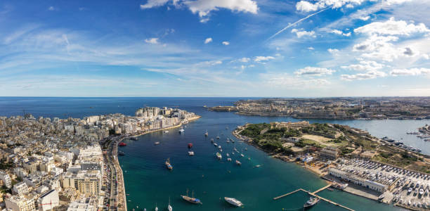 Discover Sliema and Valletta in Malta overlooking the Mediterranean Sea with boats sailing on the blue ocean Surface. Manuel Island seen in the middle. Seen a sunny day.