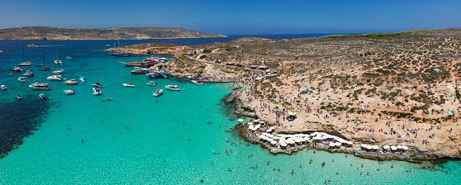 Sun-soaked Bliss: Aerial view of Comino's Blue Lagoon, Malta, on a scorching hot summer day by the Mediterranean Sea. People sunbathing and boats resting on the water surface.