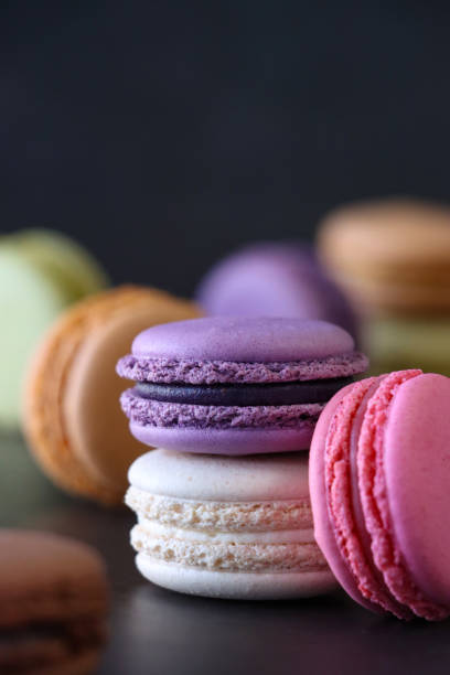 istock Close-up image of batch of macarons, multi coloured macarons filled with flavoured butter cream, blueberry, strawberry, chocolate, pistachio, vanilla, orange flavoured meringues, black background, focus on foreground, copy space 1871519658