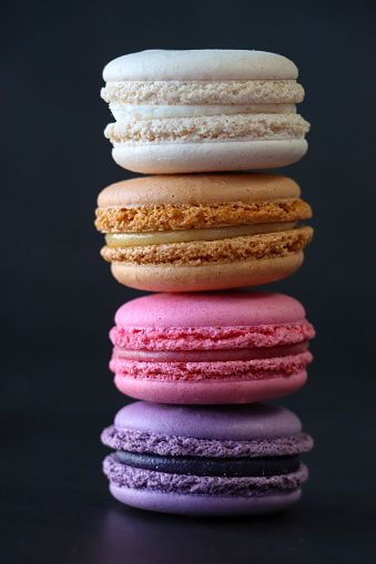 Stock photo showing close-up view of a stack of multi coloured macarons on a black background. Pink strawberry, brown chocolate, purple blueberry and white vanilla flavoured meringues.