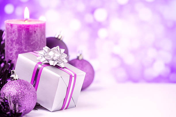 Purple Christmas baubles, a candle and a gift with a bright glittering background.