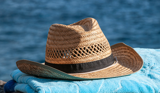 Off on vacation! Sun hat on a beach towel in front of the sea.