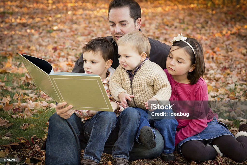 Padre leggendo a sua bambini all'aperto in autunno giorno - Foto stock royalty-free di Ambientazione esterna