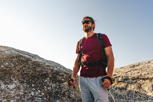 Bearded traveler with a backpack and sunglasses on the top of a mountain, portrait