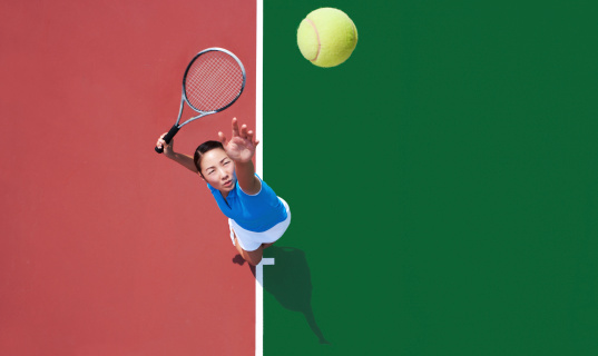 Young Asian woman serving tennis ball, photographed from directly above her.