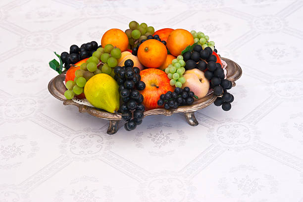 Antique Fruit Bowl Antique silver fruit bowl with colorful fruits on a dining table with a damask tablecloth. Copy space. antique fruit bowl stock pictures, royalty-free photos & images
