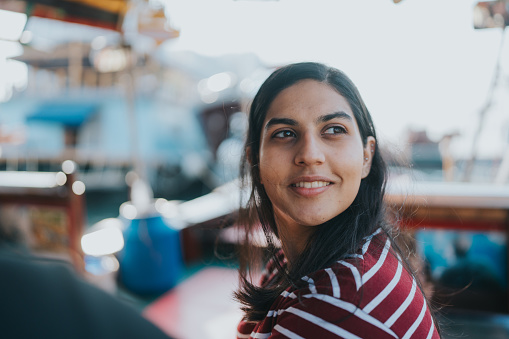 A close-up shot of an Indian female tourist looking to the wonderful sea view. She is smiling as the breeze gently blows her short black hair. She is mesmerized by the incredible view from the Sampan boat.
