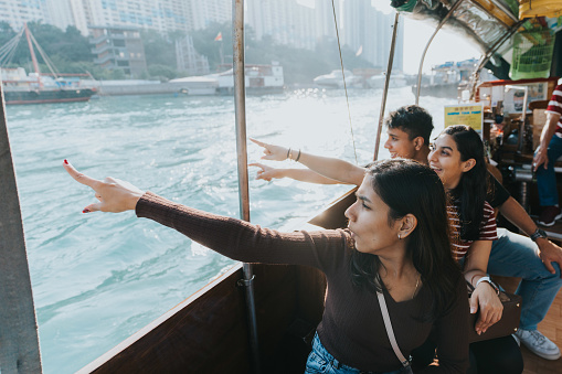 A medium shot of two Indian female tourists and an Indian male tourist pointing at something. They are really captivated and interested with the view they are currently looking.