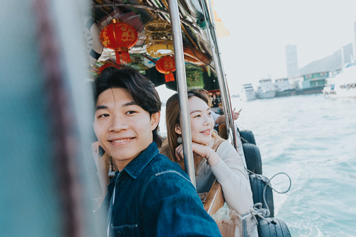 A close-up of a young Chinese couple enjoying the spectacular ocean view. The girlfriend with her hand on her chin is smiling. They look carefully to the amazing landscape, making sure they do not miss a single view.