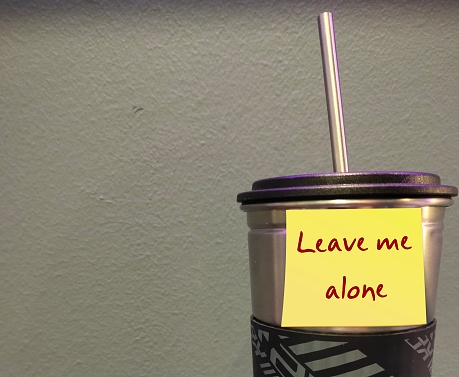 Tumbler with yellow stick note written LEAVE ME ALONE on copy space wall -  refrain from disturbing, interfering or need private time - asking other to stop bothering or go away