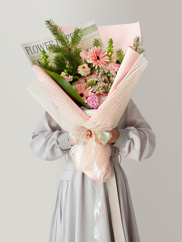 Woman in a dress holding a bouquet of flowers in front of her face. Isolated white background. Graduation, celebration, surprise event concept.