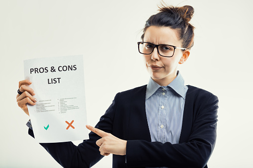 Woman with glasses holds up a list of pros and cons, clearly inclined to point out that caution is never excessive and the risks of cons exist.