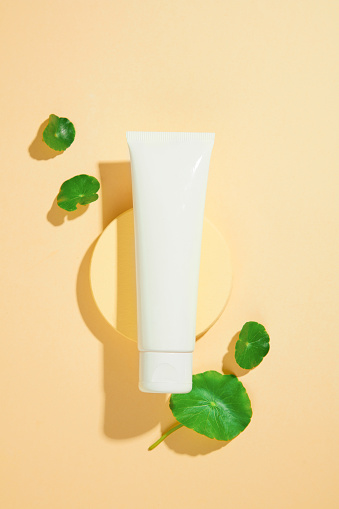 A tube of cosmetics is displayed on a round platform, surrounded by fresh pennywort leaves. Centella has the ability to inhibit the formation of melanin, reduce dark spots and even skin tone.