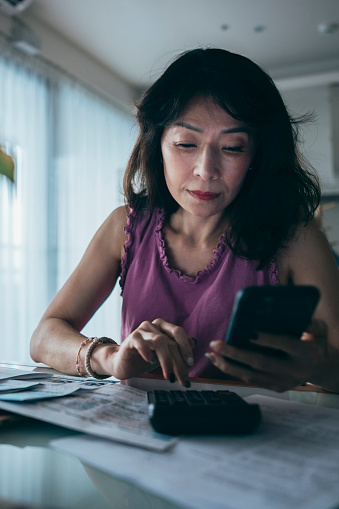 A stressed mother sits at her desk, carefully going through her finances. With a furrowed brow, she examines bills, account statements, and budget documents, reflecting the weight of financial responsibilities on her shoulders.