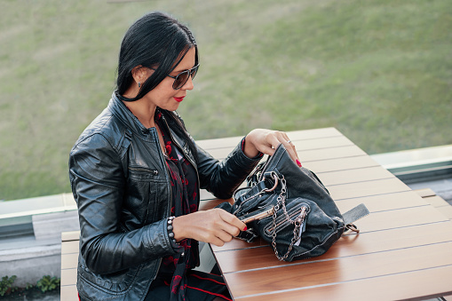 Woman with black hair sitting and looking into her bag